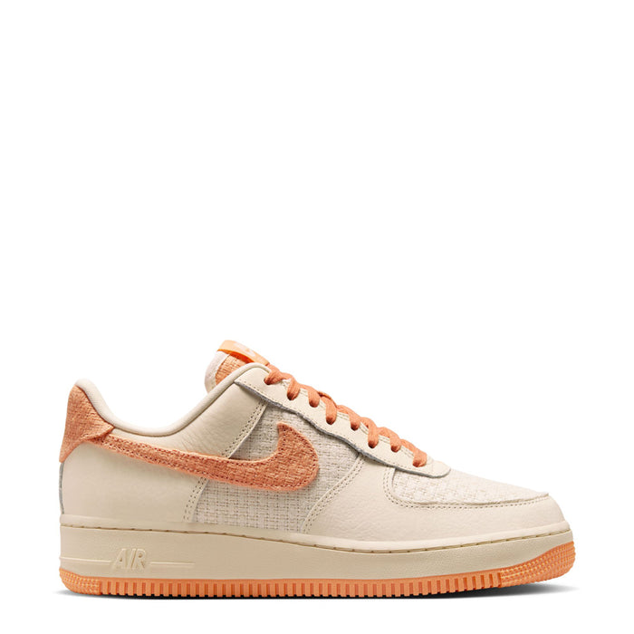 Women’s Air Force 1 low-top sneakers in cream with orange swoosh, laces, and gum sole.