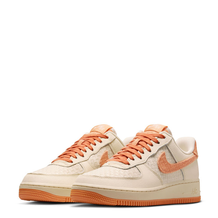 Pair of women’s Air Force 1 low-top sneakers in cream with orange accents and gum sole.