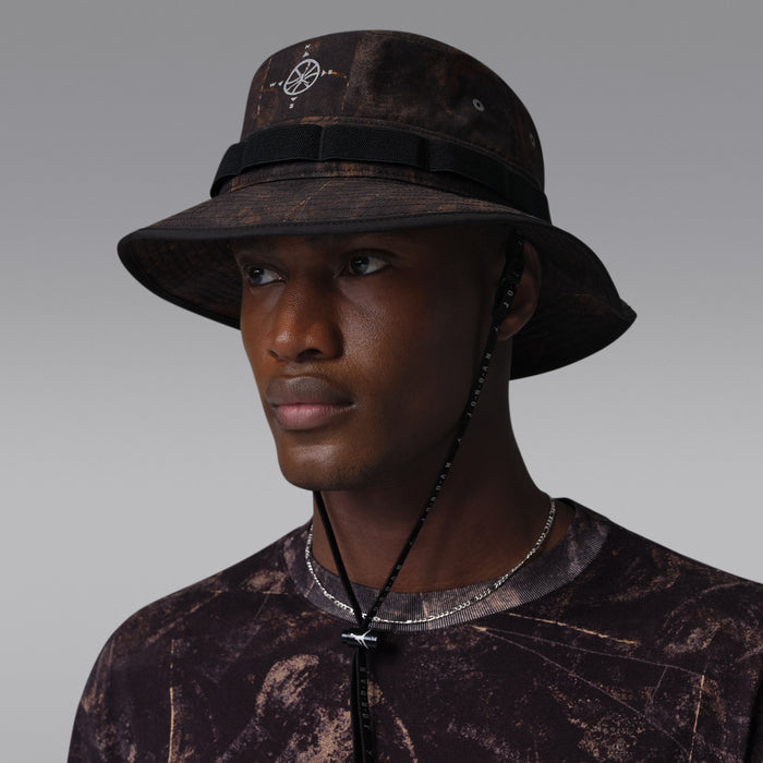 Dark brown/olive bucket hat with compass emblem, eyelets on crown, black band