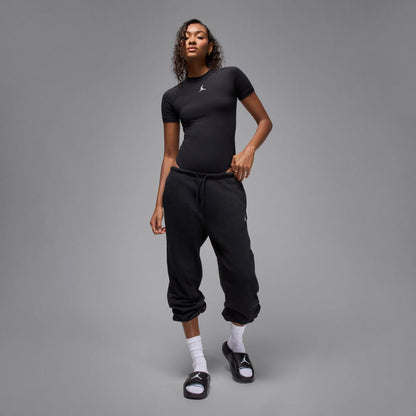 Model wearing black slide sandals with white logo; black outfit and socks visible