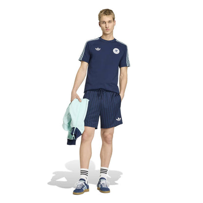 Men's navy tee with white shoulder stripes and crest logo, worn with striped shorts.