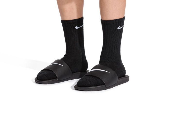 Youth slide sandals with white swoosh straps, worn with black socks