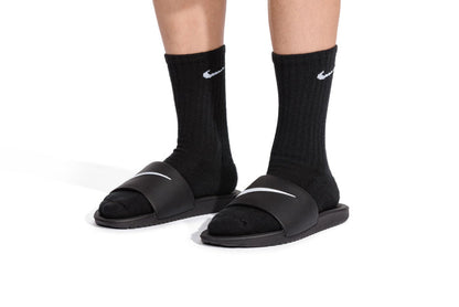Youth slide sandals with white swoosh straps, worn with black socks