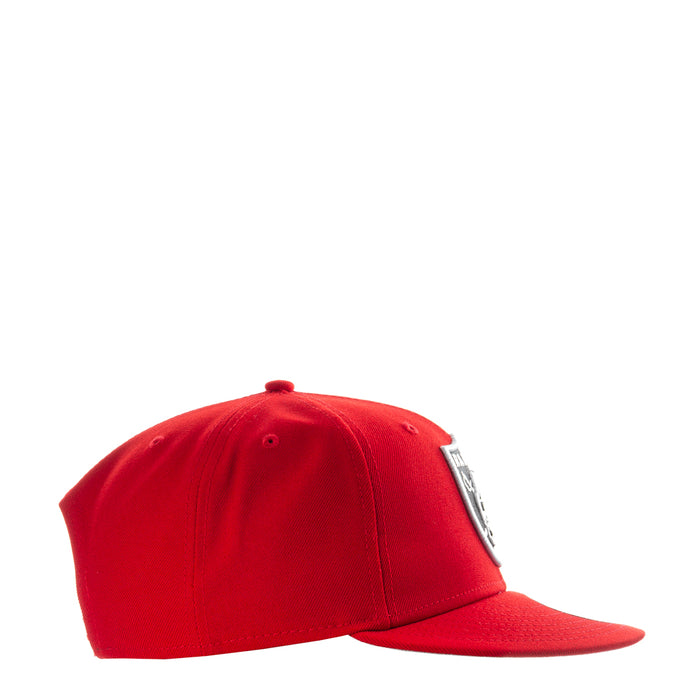 Red baseball cap side view with small Raiders logo tag