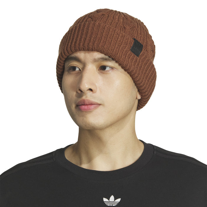Brown cable-knit beanie on model with ribbed fold and square leather-look logo patch