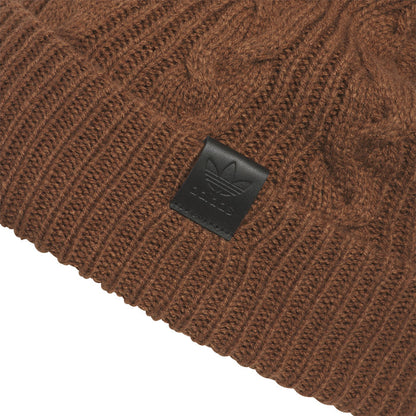 Brown cable-knit beanie close-up with square leather-look logo patch on cuff